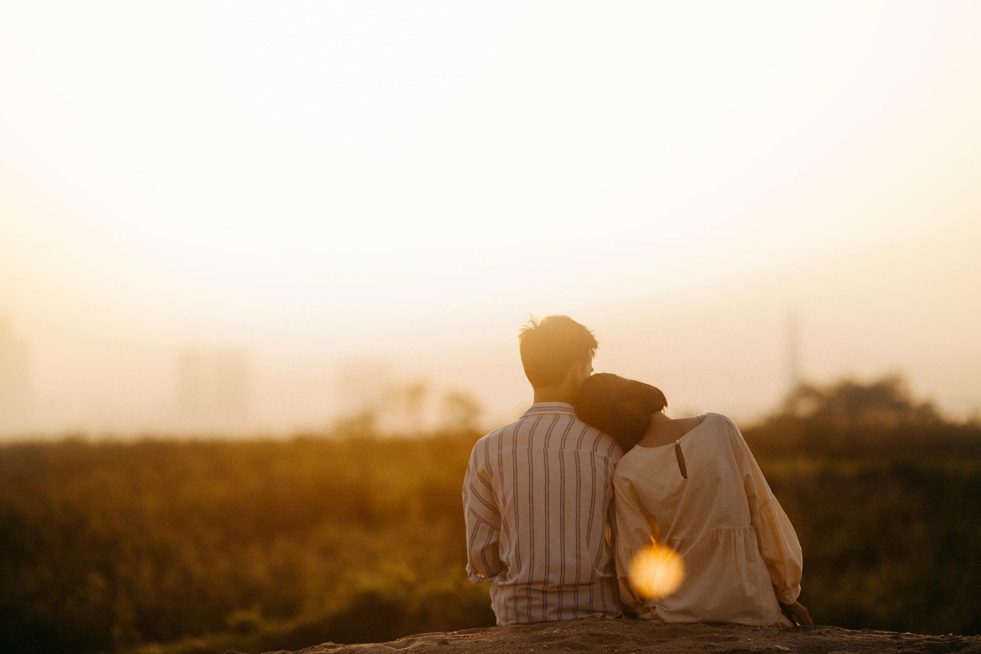 Paar sitzt auf einem Feld und schaut sich den Sonnenuntergang an; Symbolbild_Monogamie